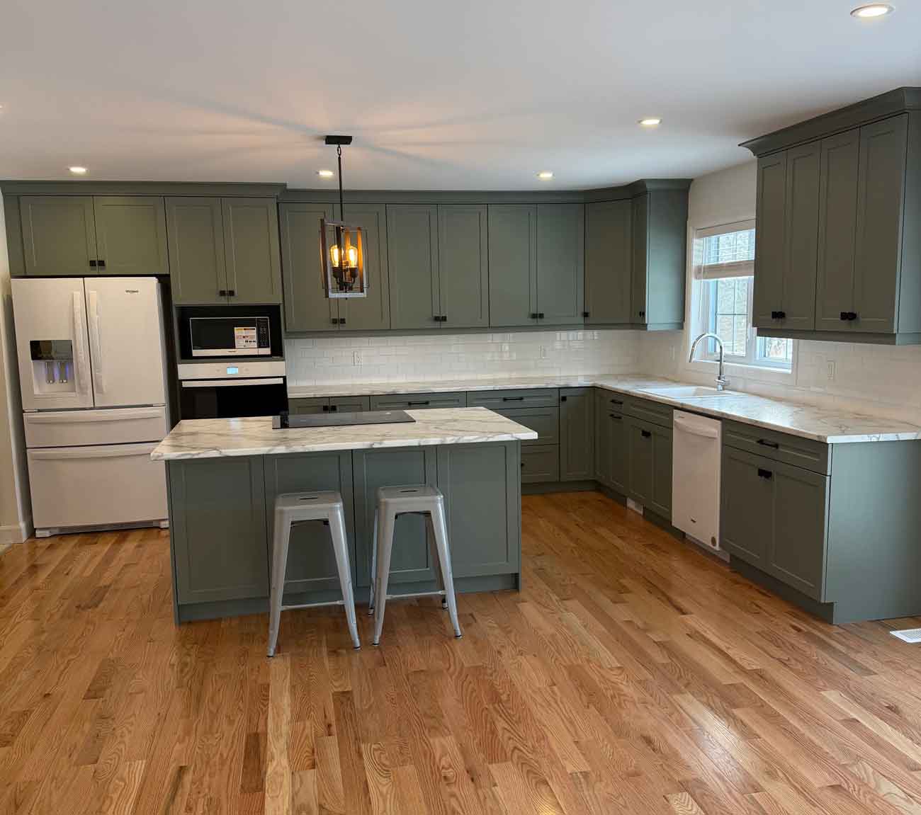Brand new kitchen with green cabinets and island. White counters, backsplash and appliances